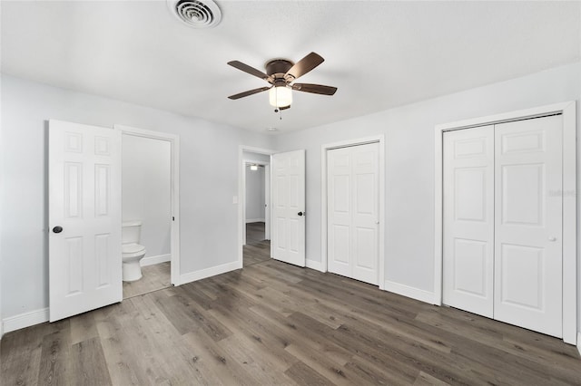 unfurnished bedroom featuring multiple closets, ceiling fan, dark wood-type flooring, and connected bathroom