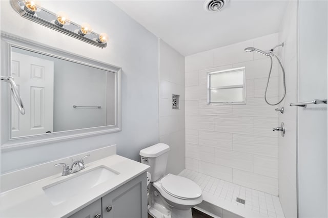 bathroom with a tile shower, vanity, and toilet