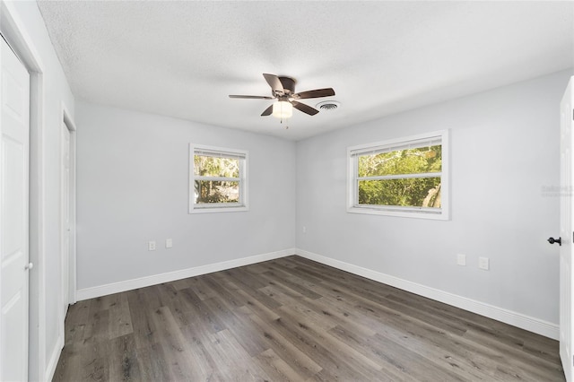 spare room featuring dark hardwood / wood-style flooring, ceiling fan, plenty of natural light, and a textured ceiling