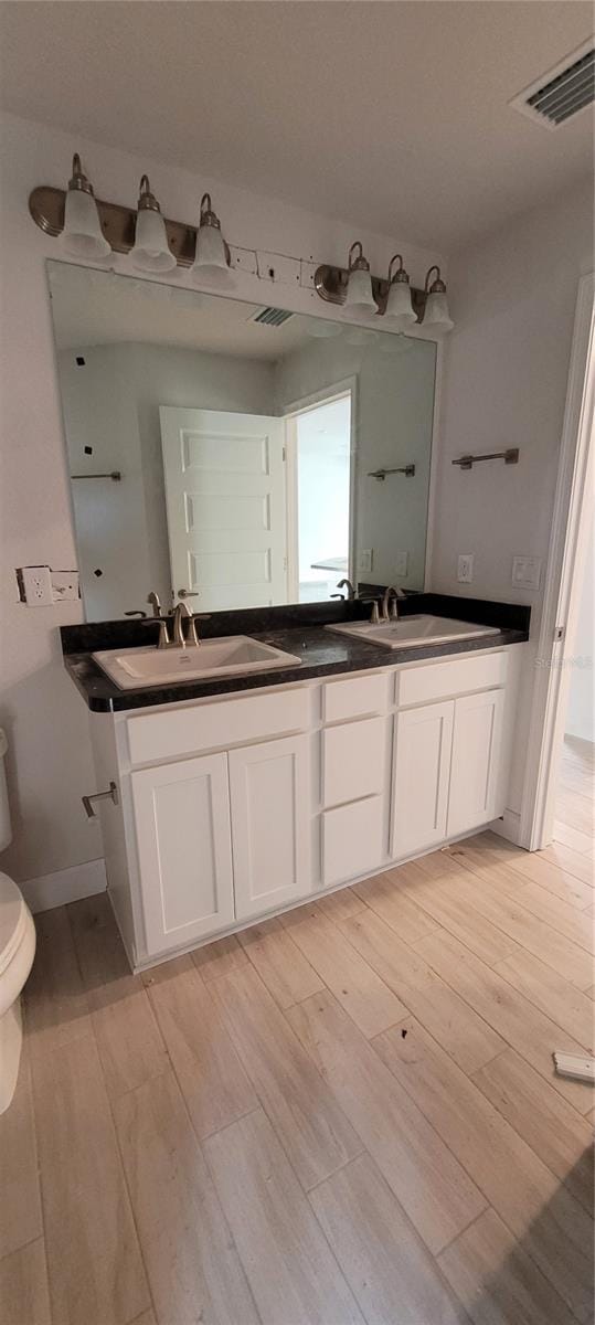 full bath with toilet, a sink, visible vents, and wood finished floors