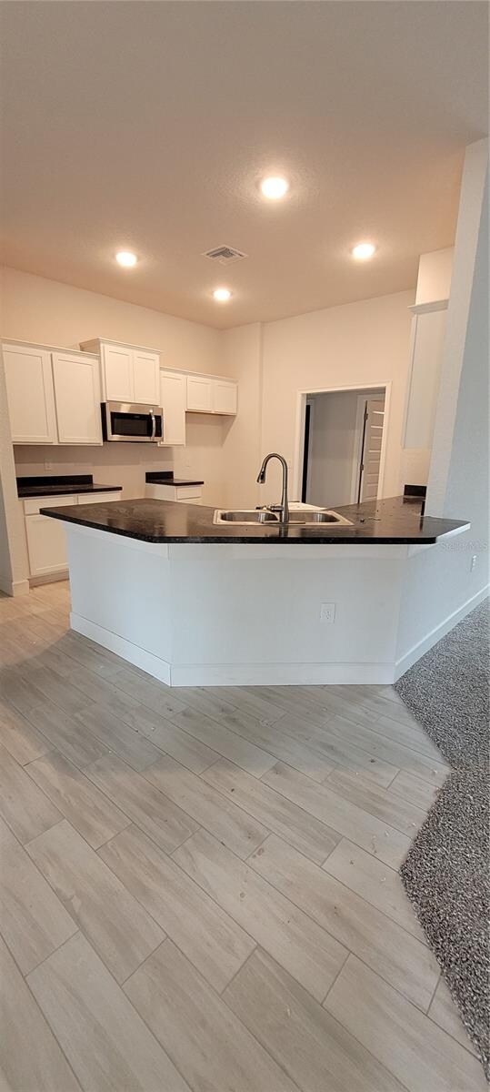 kitchen featuring visible vents, dark countertops, stainless steel microwave, white cabinetry, and a sink