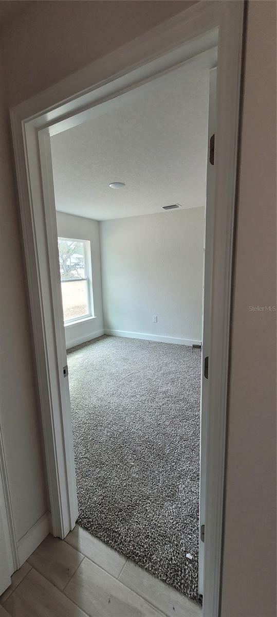 unfurnished room featuring carpet, wood finished floors, visible vents, and baseboards