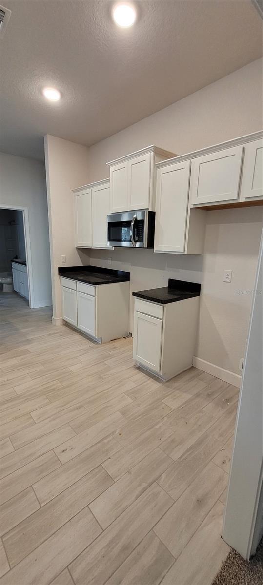 kitchen featuring light wood-type flooring, stainless steel microwave, white cabinets, and a textured ceiling