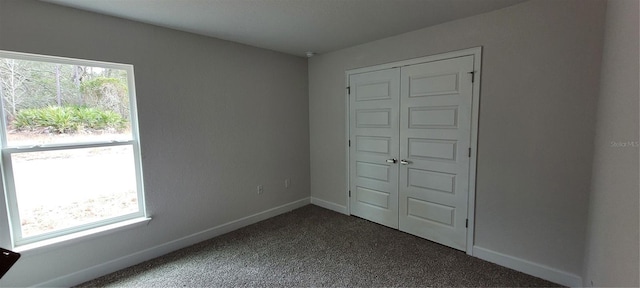 unfurnished bedroom with baseboards, dark colored carpet, and a closet