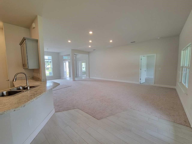 unfurnished living room with light carpet, a sink, recessed lighting, light wood-style floors, and baseboards