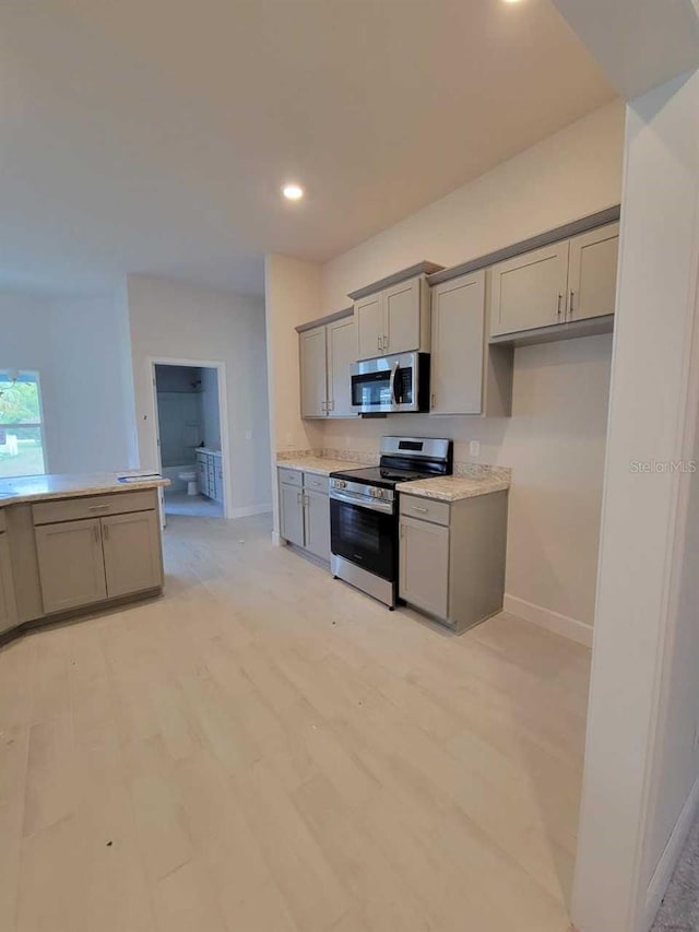 kitchen featuring baseboards, light wood finished floors, gray cabinetry, light countertops, and appliances with stainless steel finishes