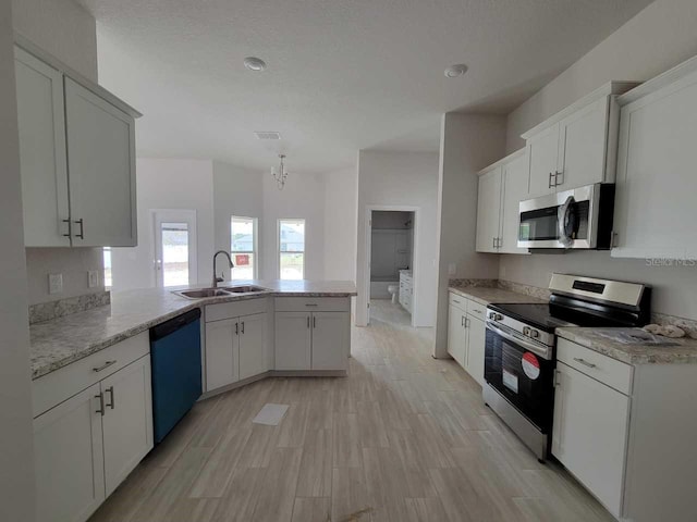 kitchen featuring visible vents, a peninsula, stainless steel appliances, a sink, and light wood-type flooring