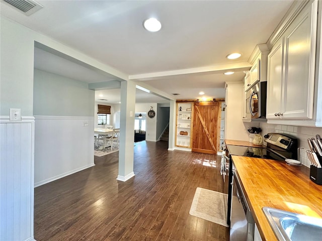 kitchen with butcher block countertops, a barn door, dark wood-type flooring, and appliances with stainless steel finishes