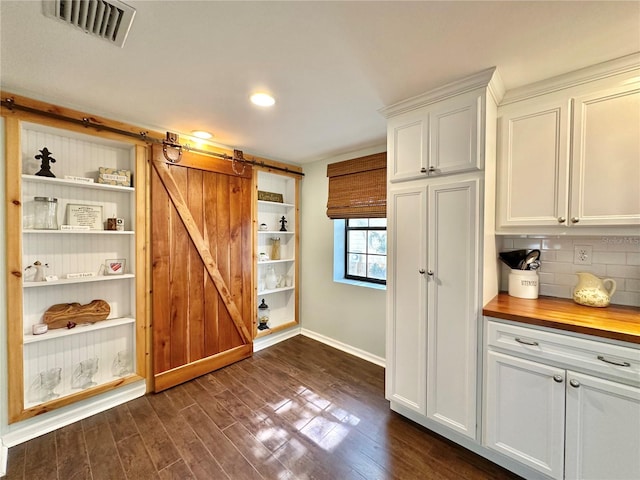 kitchen with white cabinets, decorative backsplash, a barn door, dark hardwood / wood-style flooring, and butcher block counters