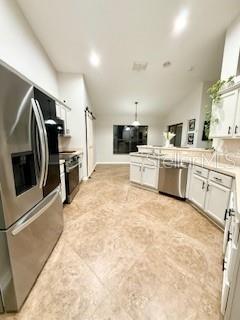 kitchen featuring white cabinetry, stainless steel appliances, kitchen peninsula, lofted ceiling, and decorative light fixtures