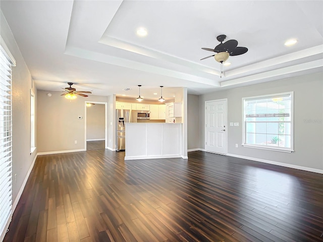 unfurnished living room featuring a tray ceiling, ceiling fan, and dark wood-type flooring