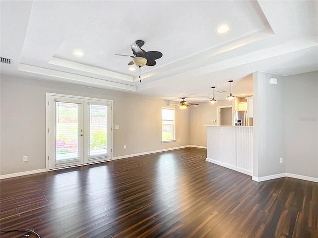 unfurnished living room featuring dark wood-type flooring, a wealth of natural light, and a tray ceiling