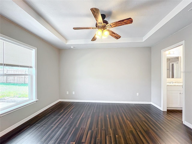 spare room with a raised ceiling, ceiling fan, and dark hardwood / wood-style flooring