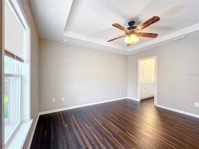 unfurnished room featuring a raised ceiling, ceiling fan, and dark hardwood / wood-style flooring