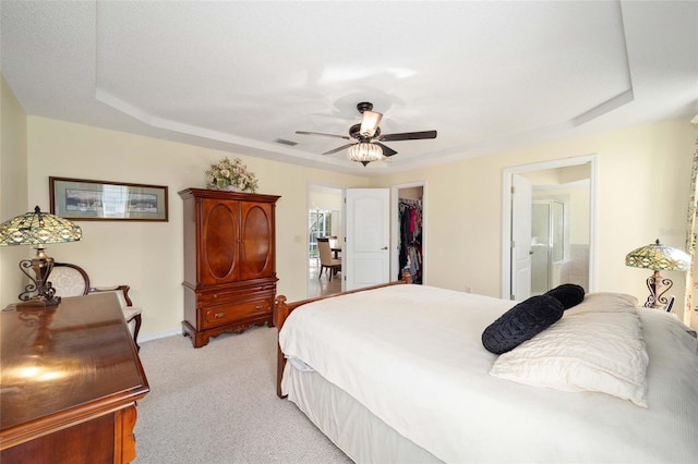 bedroom with ceiling fan, light colored carpet, a walk in closet, and ensuite bath