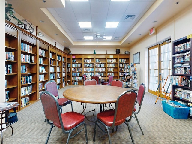 carpeted dining space with a drop ceiling, ceiling fan, and a raised ceiling