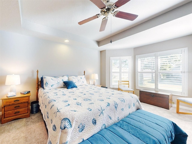 bedroom featuring ceiling fan, light colored carpet, and a tray ceiling