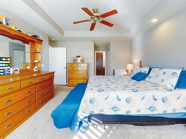 carpeted bedroom with ceiling fan, a raised ceiling, and a closet