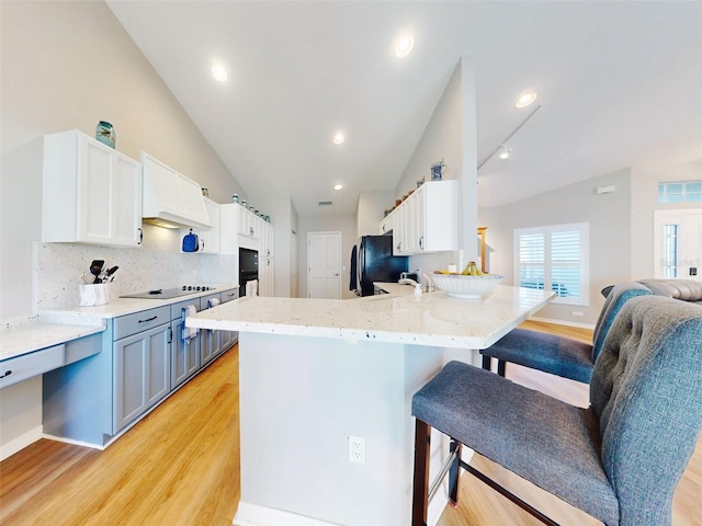 kitchen featuring kitchen peninsula, light wood-type flooring, a breakfast bar area, white cabinetry, and lofted ceiling