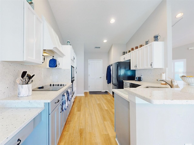 kitchen featuring lofted ceiling, white cabinets, black appliances, sink, and light hardwood / wood-style flooring