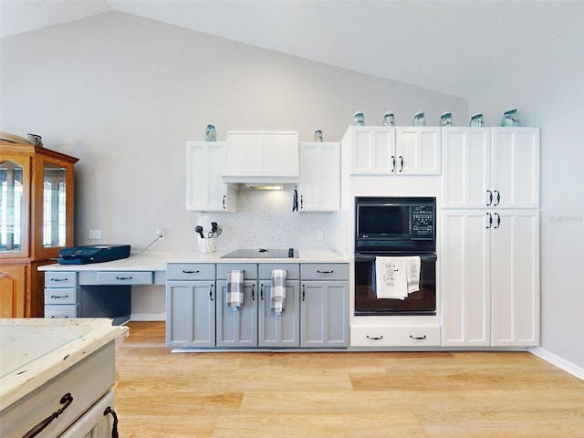 kitchen featuring white cabinetry, premium range hood, vaulted ceiling, black appliances, and light wood-type flooring