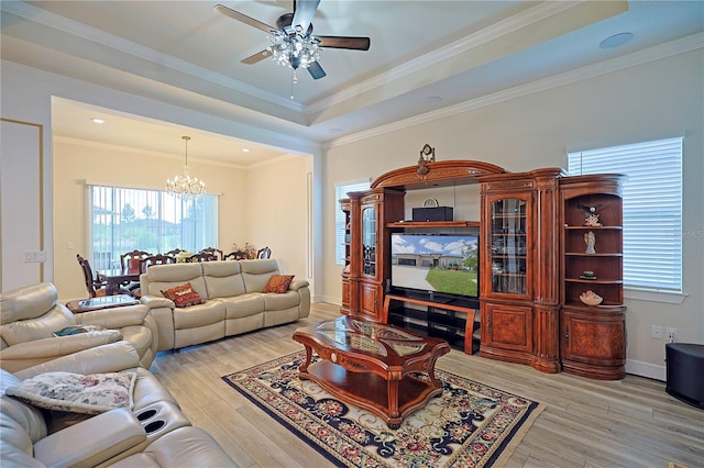 living room featuring ceiling fan with notable chandelier, a tray ceiling, light hardwood / wood-style flooring, and crown molding