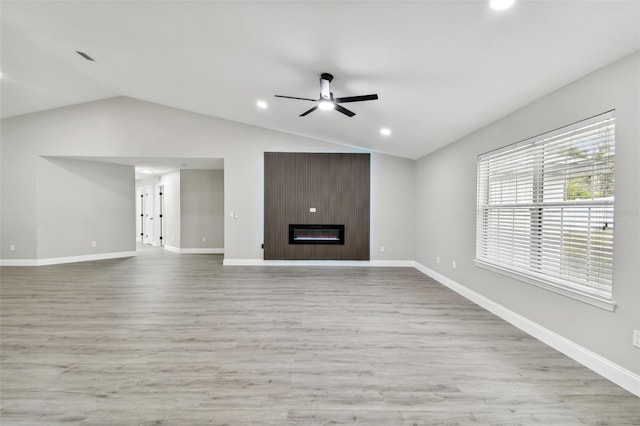 unfurnished living room with light wood-type flooring, a large fireplace, vaulted ceiling, and ceiling fan