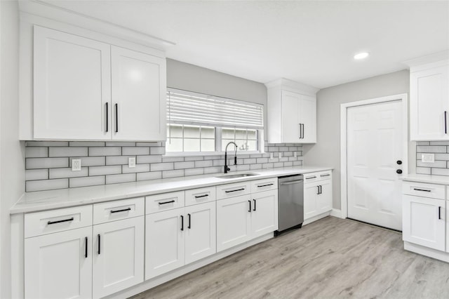 kitchen with white cabinetry, sink, light hardwood / wood-style flooring, stainless steel dishwasher, and backsplash