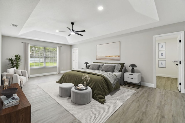 bedroom featuring a raised ceiling, ceiling fan, and light hardwood / wood-style flooring