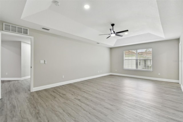 spare room featuring a raised ceiling, ceiling fan, and light wood-type flooring