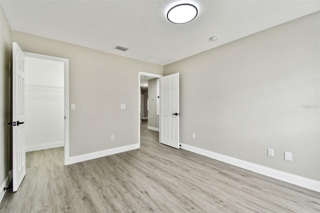 unfurnished bedroom featuring light hardwood / wood-style floors, a walk in closet, a textured ceiling, and a closet