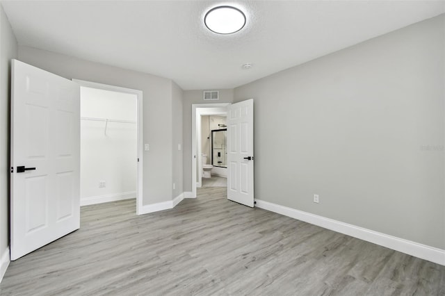 unfurnished bedroom featuring a spacious closet, a closet, and light wood-type flooring