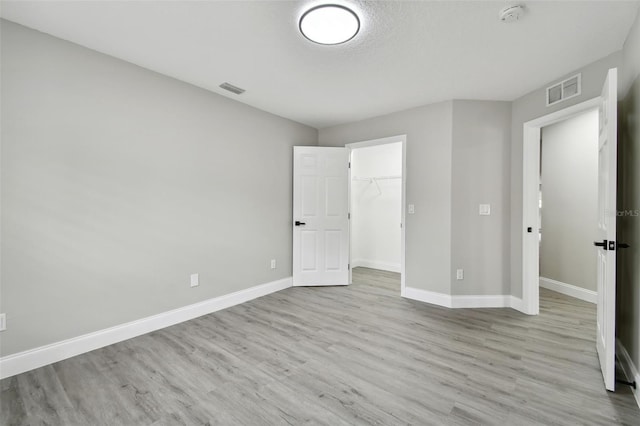 unfurnished bedroom with a closet, light hardwood / wood-style flooring, and a spacious closet