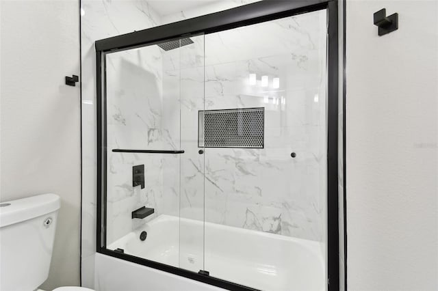 bathroom featuring toilet and shower / bath combination with glass door