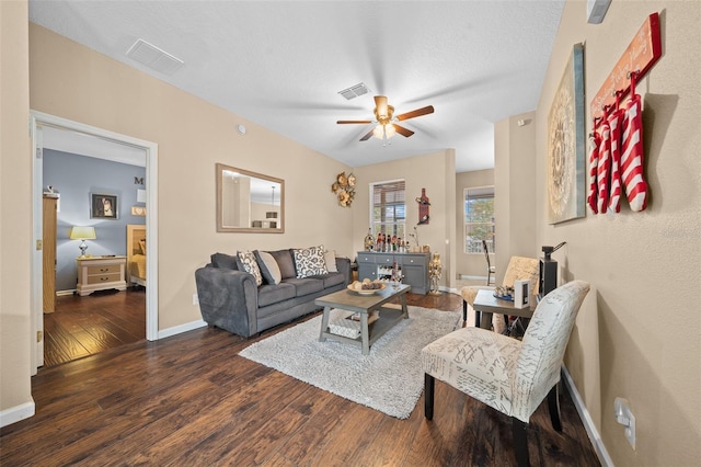 living room with a textured ceiling, ceiling fan, and dark wood-type flooring