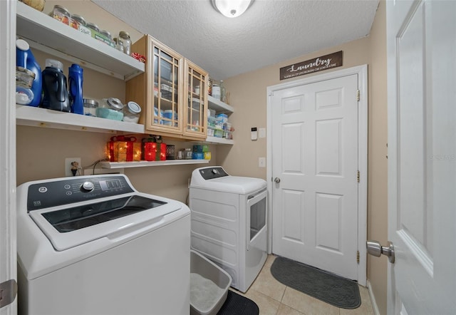 laundry room featuring washing machine and dryer, light tile patterned floors, and a textured ceiling