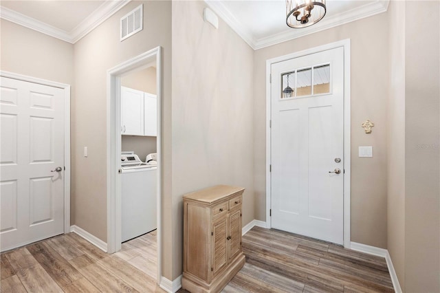 foyer with washer and dryer, an inviting chandelier, ornamental molding, and light hardwood / wood-style flooring