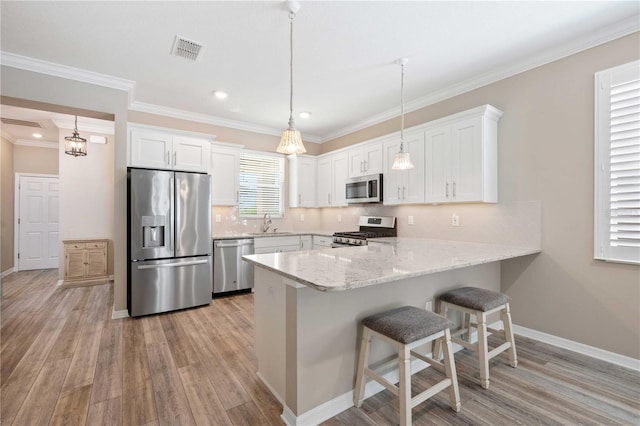 kitchen featuring stainless steel appliances, light hardwood / wood-style flooring, kitchen peninsula, decorative light fixtures, and white cabinets