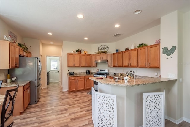 kitchen with kitchen peninsula, appliances with stainless steel finishes, light stone countertops, sink, and light hardwood / wood-style floors