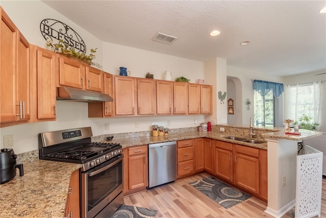 kitchen featuring sink, light stone counters, kitchen peninsula, light hardwood / wood-style floors, and appliances with stainless steel finishes