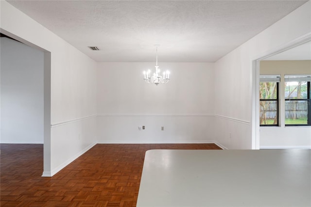 unfurnished dining area with dark parquet flooring, a textured ceiling, and an inviting chandelier