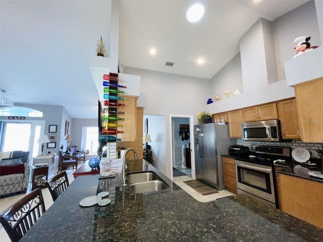 kitchen with appliances with stainless steel finishes, backsplash, sink, high vaulted ceiling, and dark stone countertops