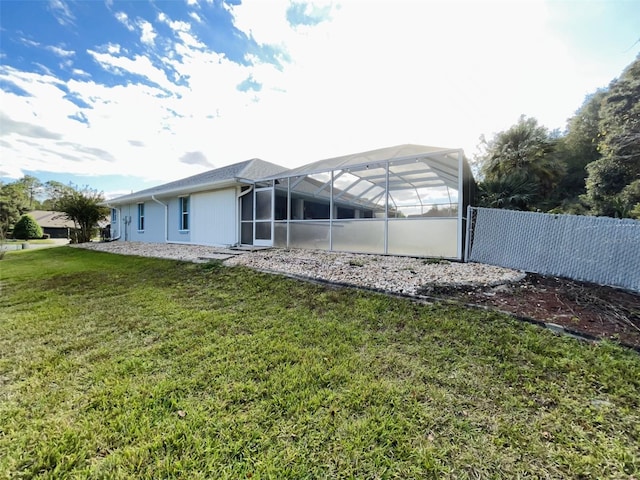 rear view of property featuring glass enclosure and a lawn