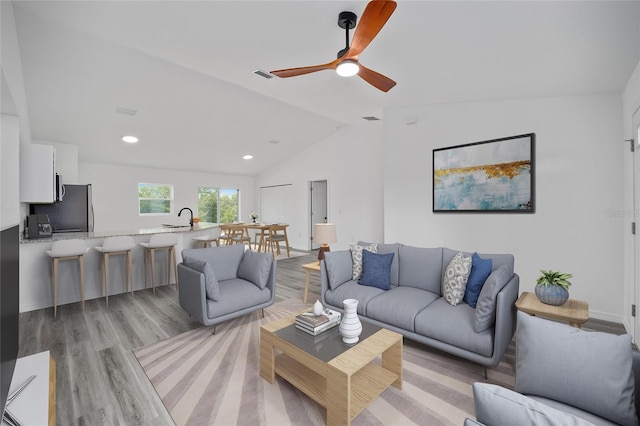 living room featuring ceiling fan, sink, vaulted ceiling, and light wood-type flooring