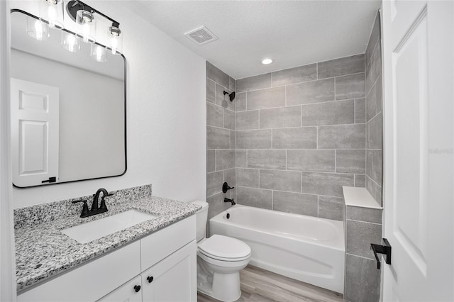 full bathroom with a textured ceiling, toilet, hardwood / wood-style flooring, vanity, and tiled shower / bath