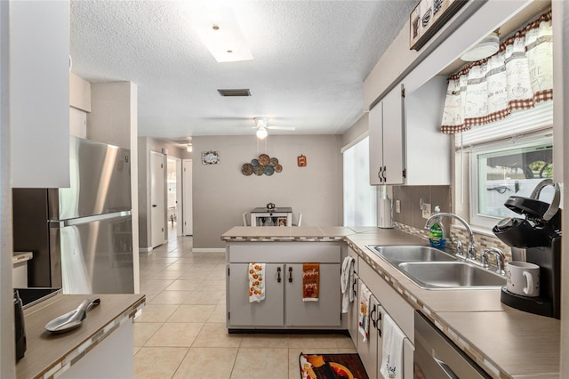 kitchen with kitchen peninsula, tasteful backsplash, sink, white cabinets, and stainless steel refrigerator