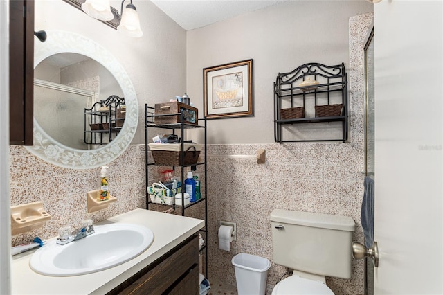 bathroom featuring a shower with door, vanity, tile walls, and toilet