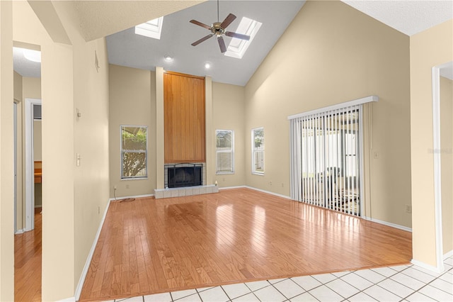 unfurnished living room with a tiled fireplace, ceiling fan, light hardwood / wood-style flooring, and high vaulted ceiling