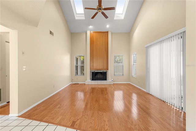 unfurnished living room featuring light wood-type flooring, a skylight, high vaulted ceiling, and ceiling fan