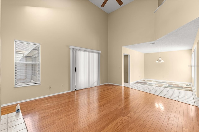 unfurnished room featuring a textured ceiling, a towering ceiling, ceiling fan with notable chandelier, and light wood-type flooring